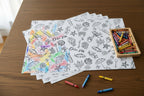 Coloring sheets with illustrations on a wooden table with crayons and a box of crayons.