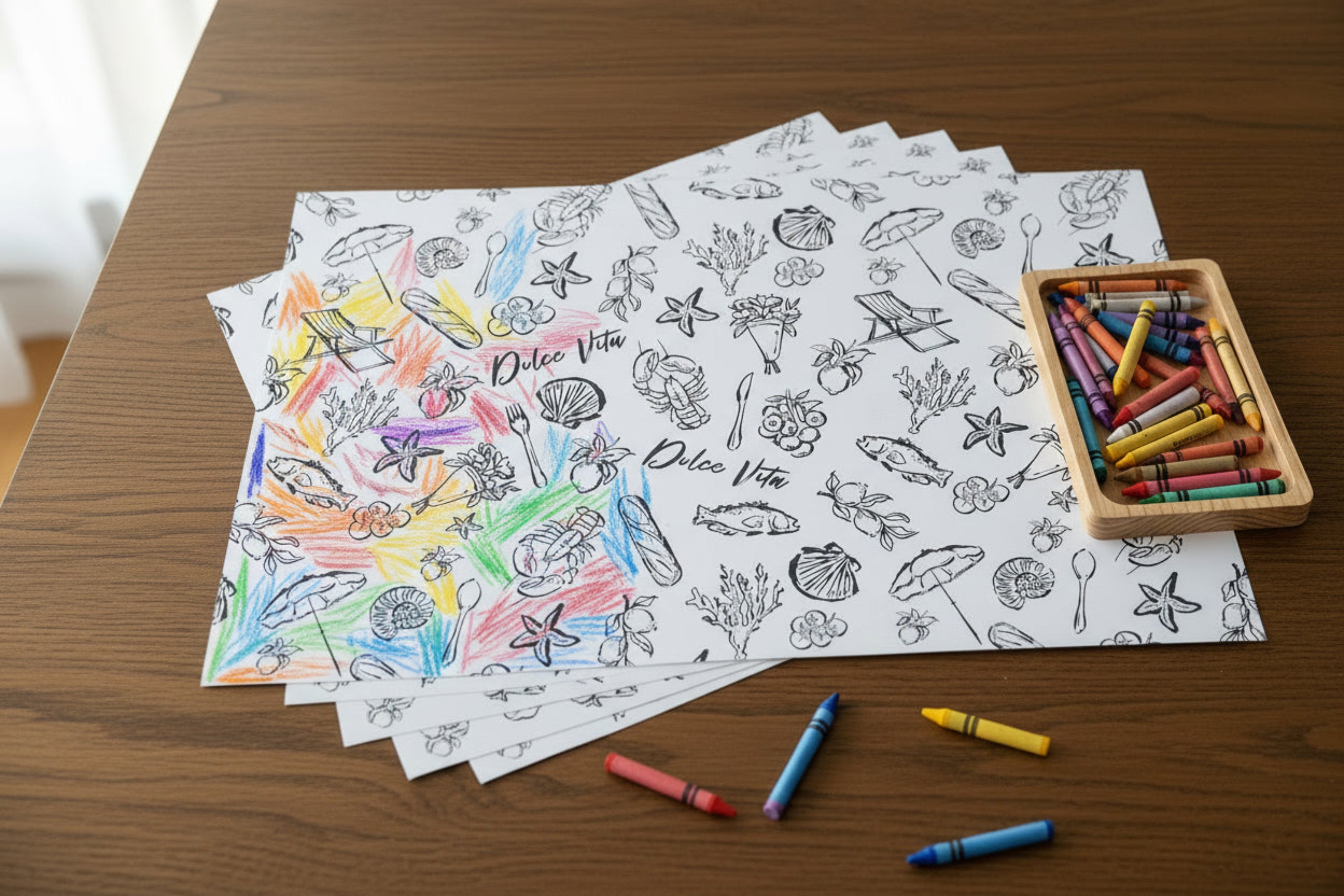 Coloring sheets with illustrations on a wooden table with crayons and a box of crayons.