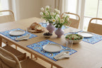 Dining table set with plates, bread, flowers, and salad in a bright room.