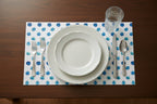 Dinnerware set on a polka dot placemat with cutlery on a wooden table.