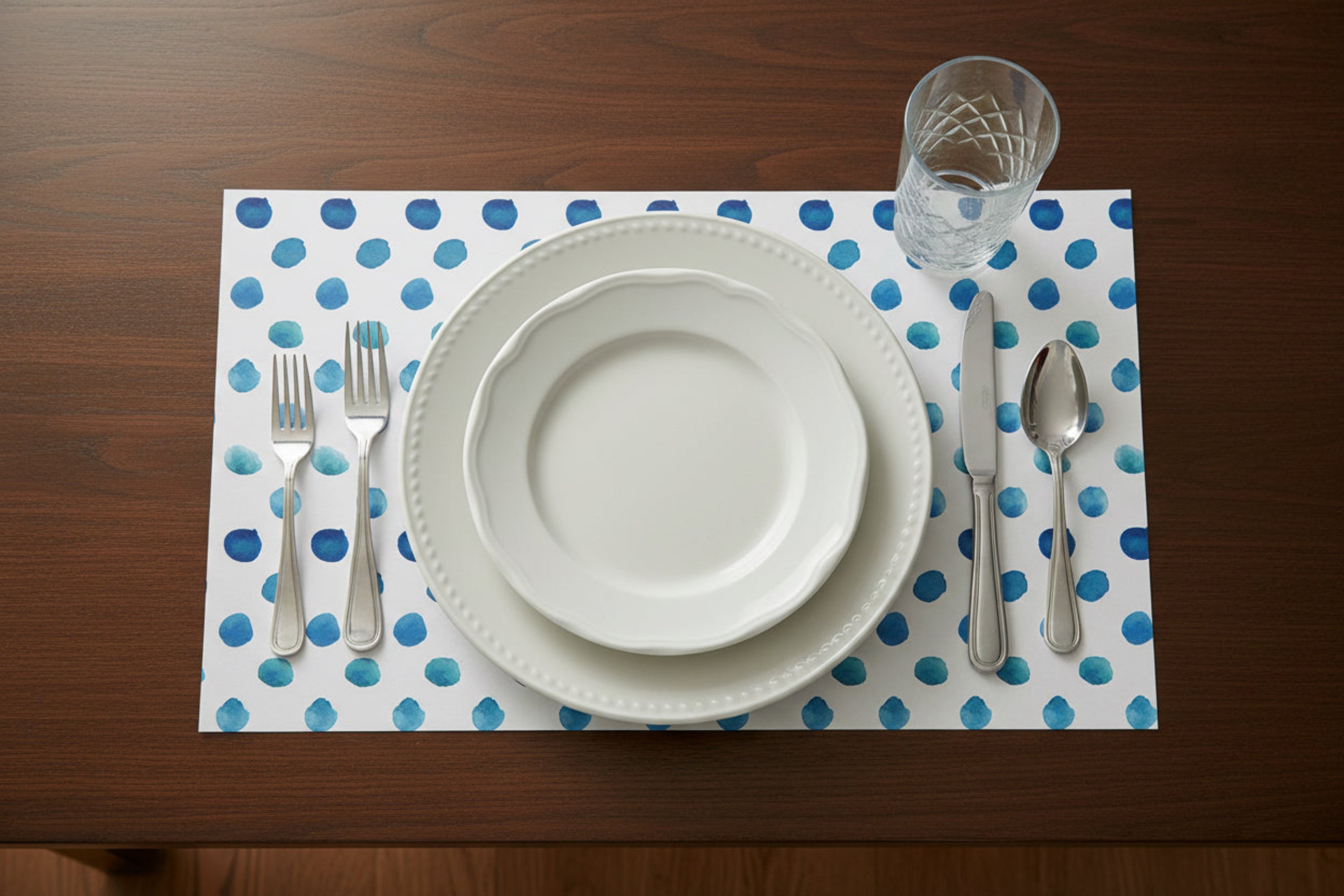 Dinnerware set on a polka dot placemat with cutlery on a wooden table.