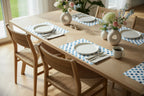 Dining table set with plates, cups, and flowers in a bright room, table set on blue polka dot watercolor paper placemats.