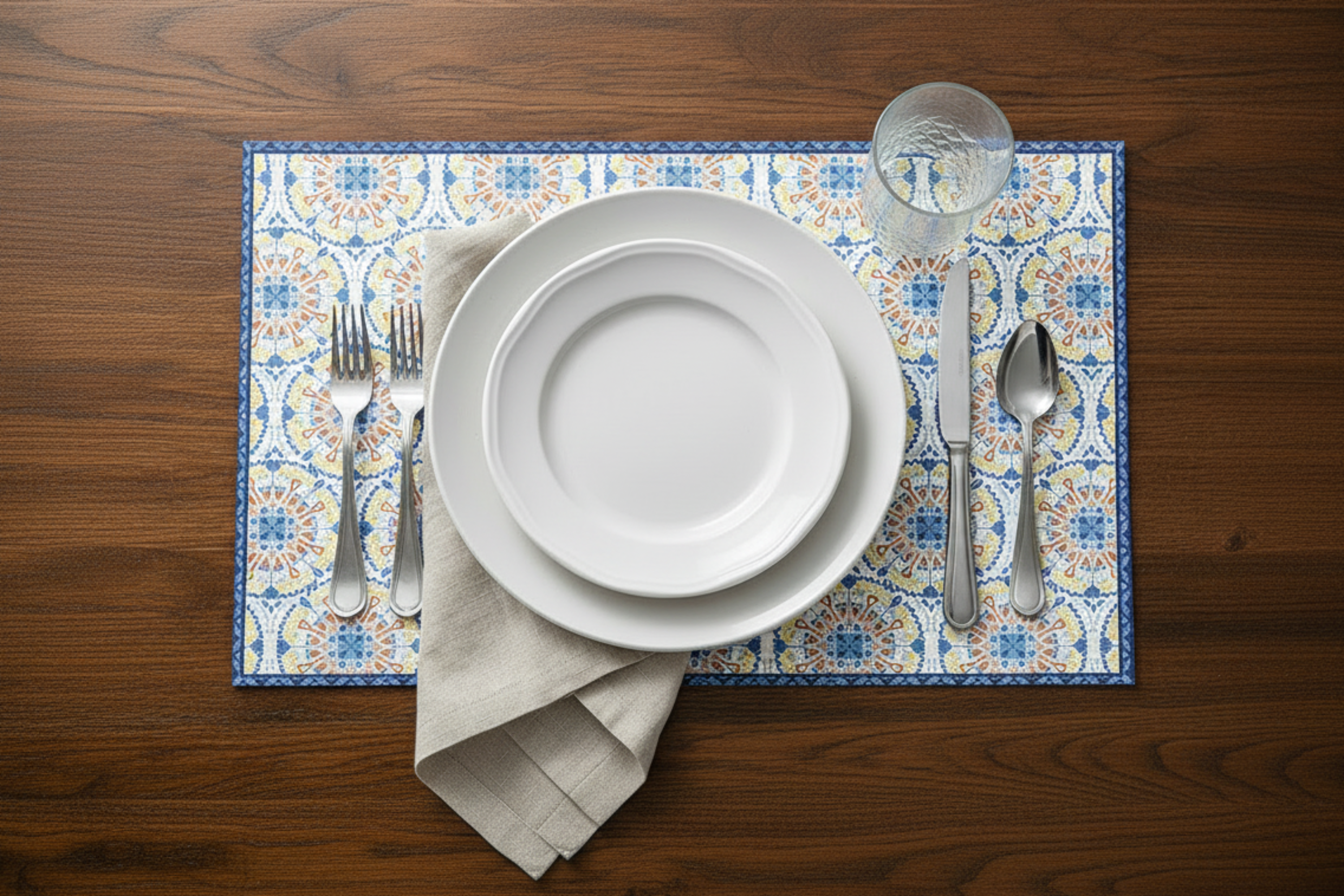 Set table with white plates, silverware, and a patterned placemat on a wooden surface
