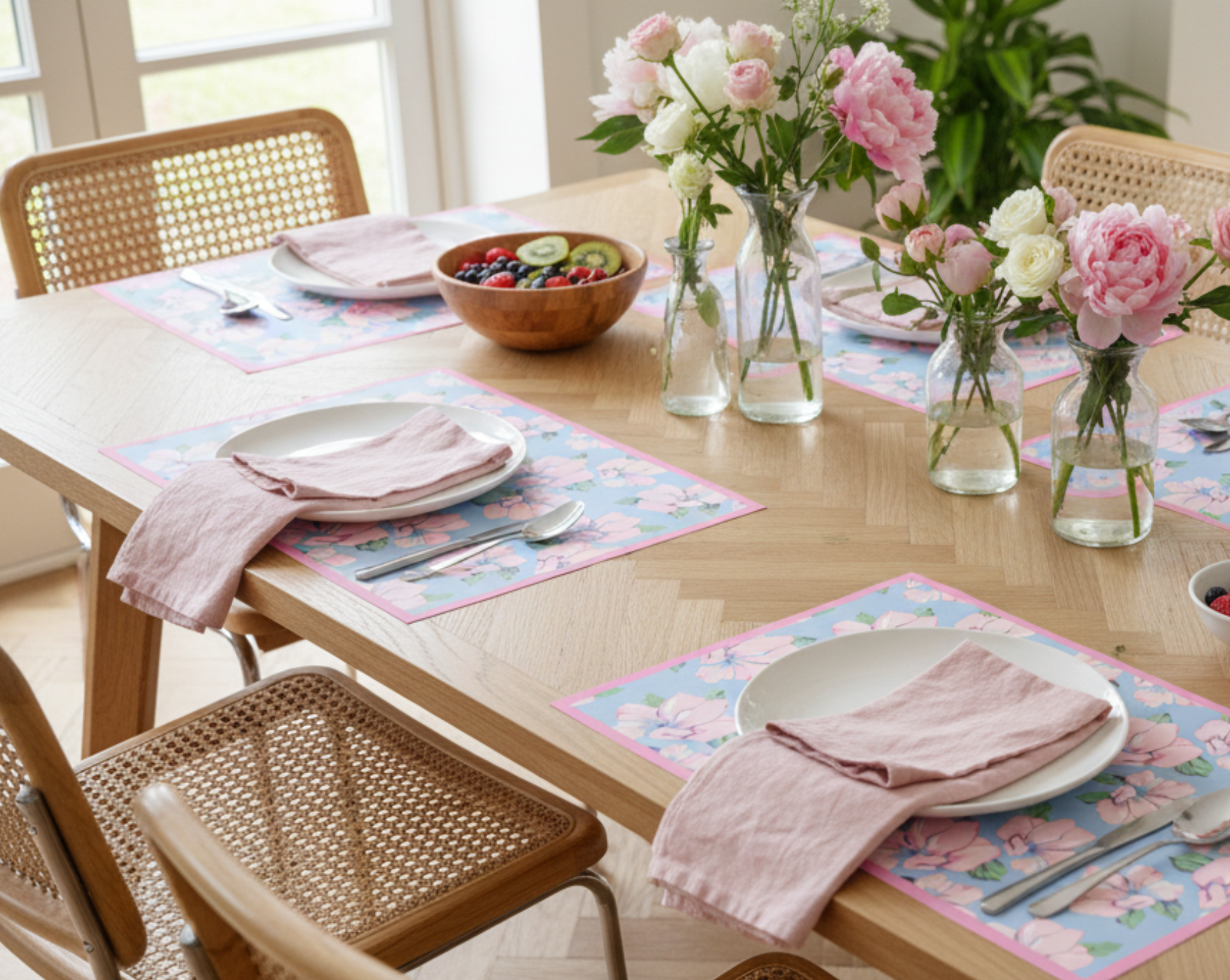 Dining table set with plates, napkins, and a floral arrangement in a bright room.