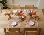 Dining table set with floral centerpieces, plates, a red checkered beachy paper placemat and chairs in a bright room.