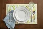 Set table with white plates, silverware, and a floral paper bunny placemat on a wooden surface