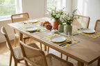 Dining table set with plates, cutlery, and flowers in a bright room with yellow evil eye inspired paper placemats.