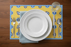 Pattern of blue eye shapes on a yellow background against a wooden table and plate setting