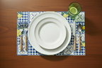 Set table with white plates, silverware, and a glass on a decorative lemon tile placemat.