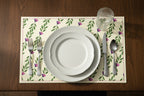 Set table with white plates, silverware, and a decorative placemat on a wooden table.