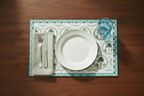 Dining setup with a white plate, fork, knife, napkin, and glass on a decorative placemat.